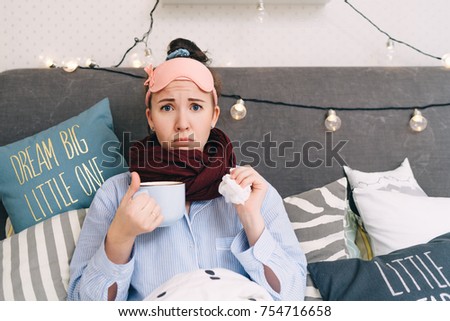 young sick woman lies in bed with cup of hot tea and tissue Royalty-Free Stock Photo #754716658