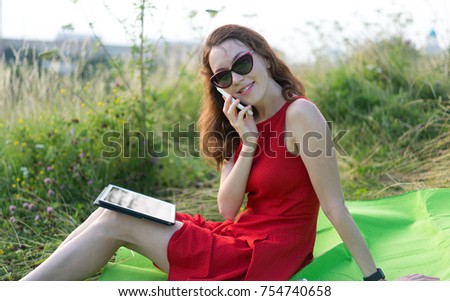 Happy young modern smiling business women in red dress and sunglasses with tablet computer and mobile phone in hands, talking on the phone