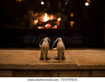 A bride's fashionable high heels sit in front of a cozy, warm fireplace.
