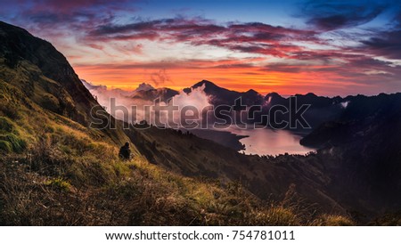 Beautiful sunset over ranges of mountains taken at Sembalun Crater rim - Mt.Rinjani, Indonesia. Male hiker/tourist is watching the sunset in the picture.