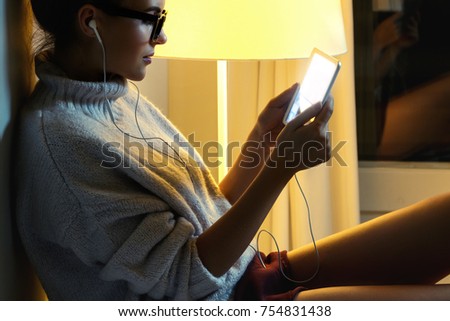 Young woman wearing a warm pullover is using tablet PC in the middle of the night