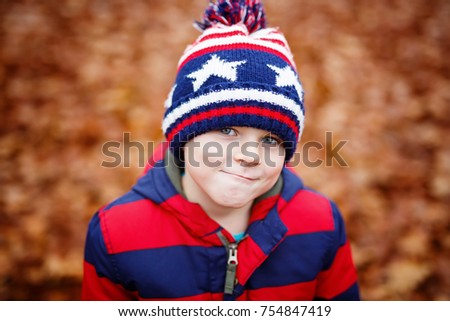 Portrait of happy cute little kid boy with autumn leaves background in colorful clothing. Funny child having fun in fall forest or park on cold day. Casual fashion for winter children clothes