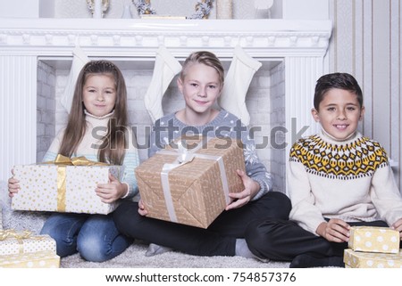 Group of three children. Merry Christmas and Happy Holidays concept. Family holiday. New Year's picture of brothers and sister. Children opening a gift at home. Friends are interested and amazed. 