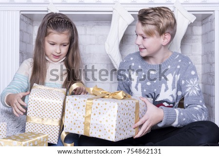 Merry Christmas and Happy Holidays concept. Portrait of little boy and girl. Family holiday. New Year's picture of brother and sister with gifts. Children opening a gift at home in the living room. 