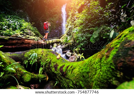 Freedom Young traveler woman with 
Red Backpack travel into amazing beautiful waterfall in tropical rain  forest at Nakornnayok , Thailand and taking a photo with smartphone 