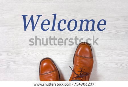 Classic men's elegant shoes standing on a white wooden floor with a blue welcome sign written on it