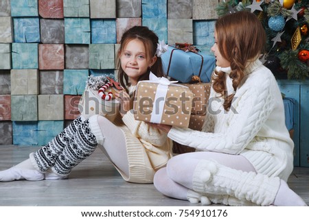 Cute girls sitting next to the Christmas tree with boxes of presents