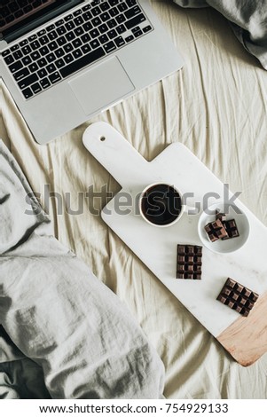 Laptop, pastel linens, breakfast with coffee and chocolate on marble cutting board. Flat lay, top view lifestyle concept.