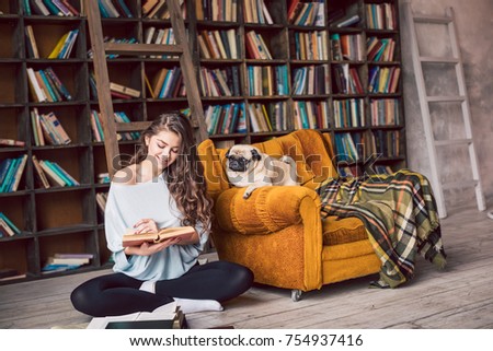 Cute reading lovers family. Beautiful woman sitting on the floor in the library and her lovely dog pug looking to the book too. Happy home weekend moment Royalty-Free Stock Photo #754937416
