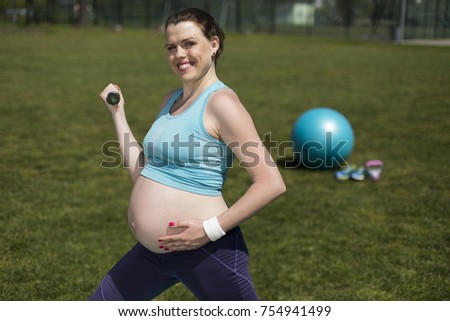 Pregnant woman doing fitness exercise on the grass