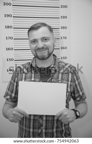 Portrait of a man with a beard on the background grid to measure growth. Man holds a plate for inscriptions. Happy adult man with a beard and mustache, smiling and looking at the camera. Wanted