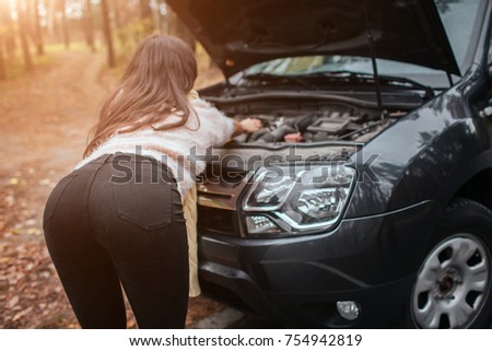 Confused young woman looking at broken down car engine ? car repair on the street