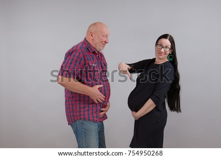 Young pregnant woman and elderly grandfather posing on gray background
