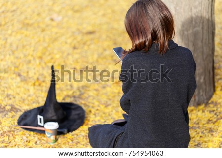 A girl in an autumn park sits in the phone, with a witch hat