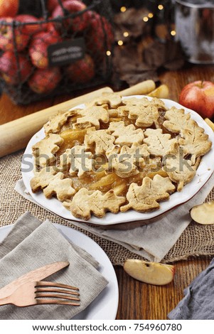 Freshly baked apple pie with top crust cut into autumn leaves shape. Apples in background.
