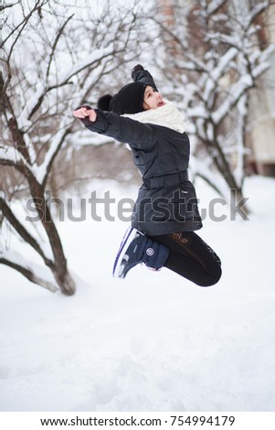 The girl jumped up against the background of trees with branches in the snow.
