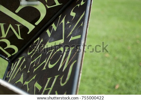background: rusty corroded iron plate (sheet), brown shades, with series of letters of alphabet carved in metal panel, through the holes of letters passes green color of the lawn, handmade, Italy