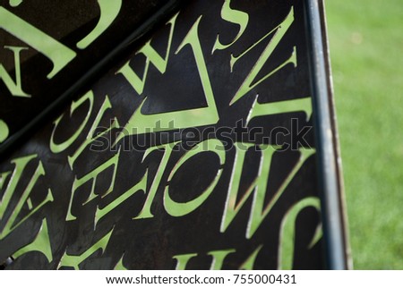 background: rusty corroded iron plate (sheet), brown shades, with series of letters of alphabet carved in metal panel, through the holes of letters passes green color of the lawn, handmade, Italy