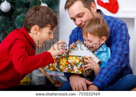Happy father and his sons at home near the Christmas tree open a gift
