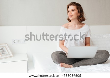 Picture of young beautiful woman sitting indoors using laptop computer. Looking aside.