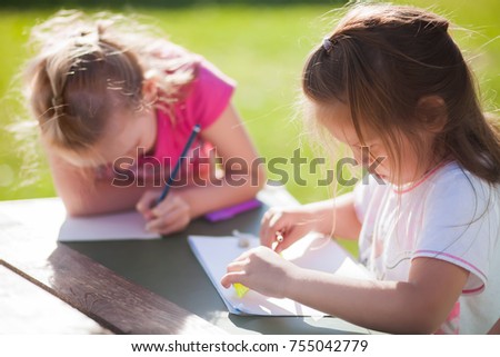 Two cute little sisters drawing. Creative kids painting together. Girls doing homework outdoors, summer day.