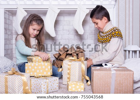 Merry Christmas and Happy Holidays concept. Portrait of little boy and girl. Family holiday. New Year's picture of brother and sister with gifts. Children opening a gift at home in the living room. 