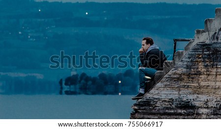 Man sitting at the dock in twilight, thinking about the meaning of life. Lake, headland with church and hills in the background.  Royalty-Free Stock Photo #755066917