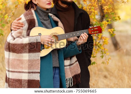 A girl is playing on a ukulele near a close-up guy on an autumnal blurred background