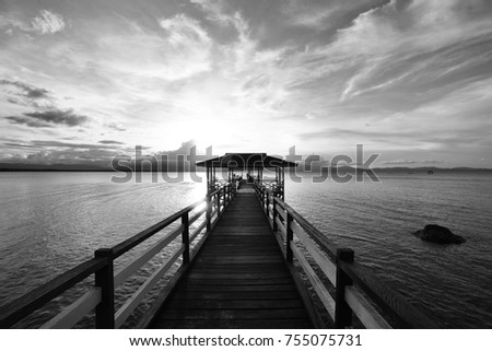 Old wooden jetty, pier on the sea. Raining from dramatic sky with dark, heavy clouds. 
