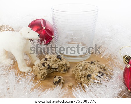 Beautiful Christmas background scene picturing a glass of milk and cookies partially eaten set out for Santa with white garland and shiny red, silver, and gold ornaments and plastic polar bear toy.