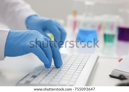 Employee chemical laboratory teacher chemist knocks his fingers keyboard makes notes electronic journal records the analysis data from reactions examining test tubes with the substance arm in gloves. Royalty-Free Stock Photo #755093647