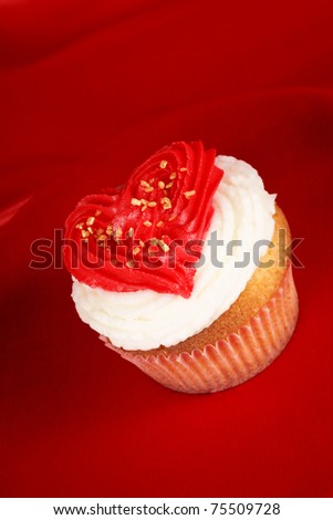 Fancy Valentine's day cupcake frosted with a red heart shape over a red background. With copy-space.