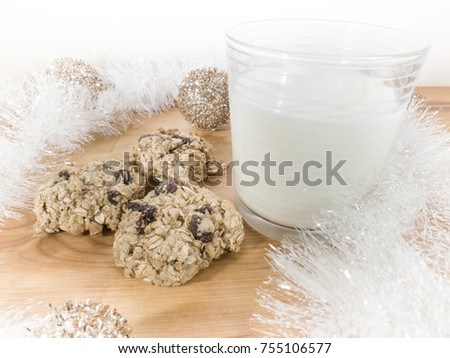 Beautiful holiday backdrop scene picturing a full glass of milk and cookies set out for Santa on Christmas night with white garland and silver and gold ornaments on butcher block table background.