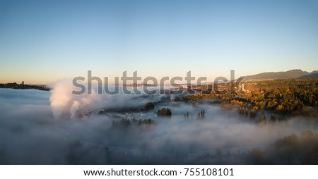 Beautiful aerial panoramic view of the ocean inlet covered in fog during a colorful sunrise. Taken in North Vancouver, British Columbia, Canada.