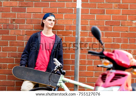 Teenage boy with skateboard standing next to the wall