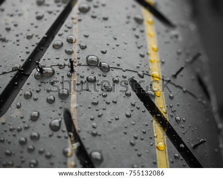 Close up shot of water drops on brand new motorcycle tire with red and yellow stripes mark on the surface. Close up shot shows the thread on the tire and also front mudguard of the motorbike.
