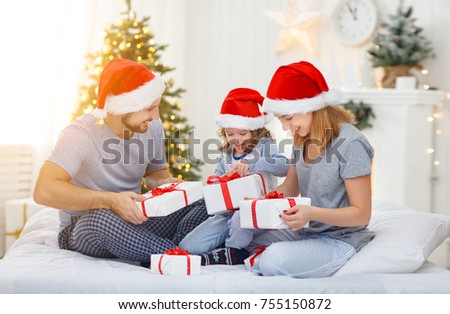 happy family mother father and child on Christmas morning in bed in pajamas open gifts