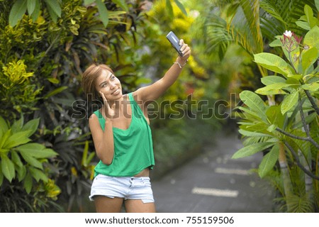 young sweet and pretty Asian woman holding mobile phone taking selfie picture in tropical jungle smiling happy posing cool in social media self portrait concept and excursion holiday trip