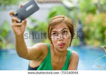 young attractive and happy Asian woman taking selfie picture for social media internet app on mobile phone camera relaxed at resort swimming pool in communication and holiday vacation relax
