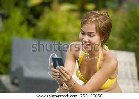 young attractive and happy Asian woman in bikini using social media internet app on mobile phone relaxed at resort swimming pool in communication and holiday vacation relax concept