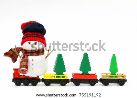 Snowman sit on the red wooden train. Snowman wear red and black knitting beanie hat and brown plaid scarf, arms made from sticks. Wooden christmas tree put on the wooden train toy alongside of snowman