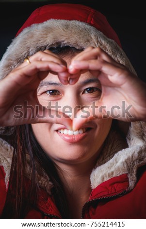 an Asia woman in the red coat make heart shape  hand  and smile with happy.