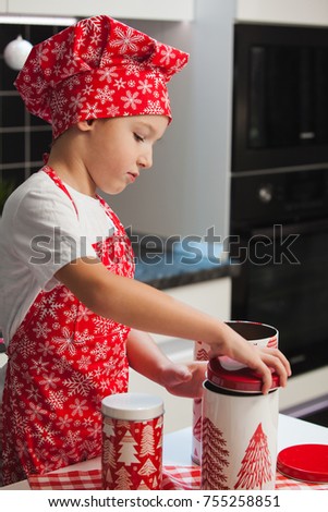 The boy in the Christmas cap of the cook and apron helps her mother cook cookies with ginger in a light kitchen with cans of New Year's pictures.  happy family, preparing for the holiday.