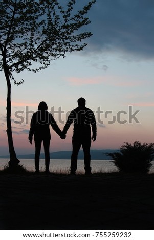 young couple standing hand in hand at sunset on the lake shore