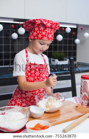 The boy in the Christmas cap of the cook and apron helps her mother cook cookies with ginger in a light kitchen with cans of New Year's pictures.  happy family, preparing for the holiday.
