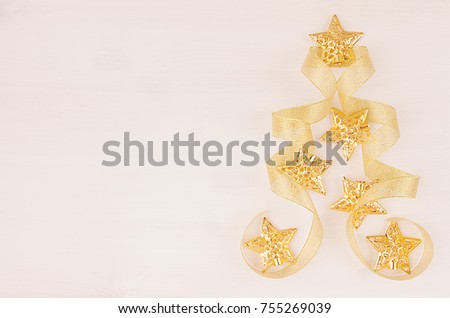 Christmas tree of gold stars, curl ribbons on soft white wood board, top view, copy space.