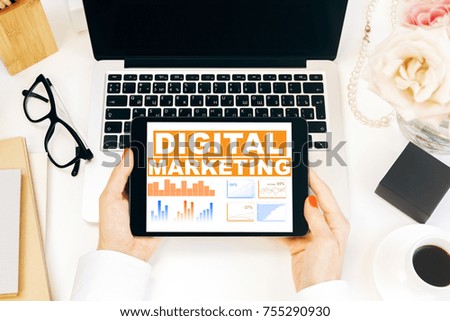 Top view of female hands holding tablet above workplace with laptop, coffee cup and other items. Digital marketing and financial growth concept 