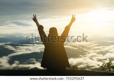 Beautiful women sitting and show victory sign on the branch and viewing mist around the scenery with sun light in the morning.