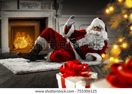 Santa Claus on floor. blurred christmas tree. Dark wooden wall with fireplace in room. 