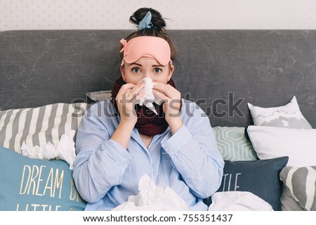 Young sick woman in bed with flu and cold blowing her nose Royalty-Free Stock Photo #755351437